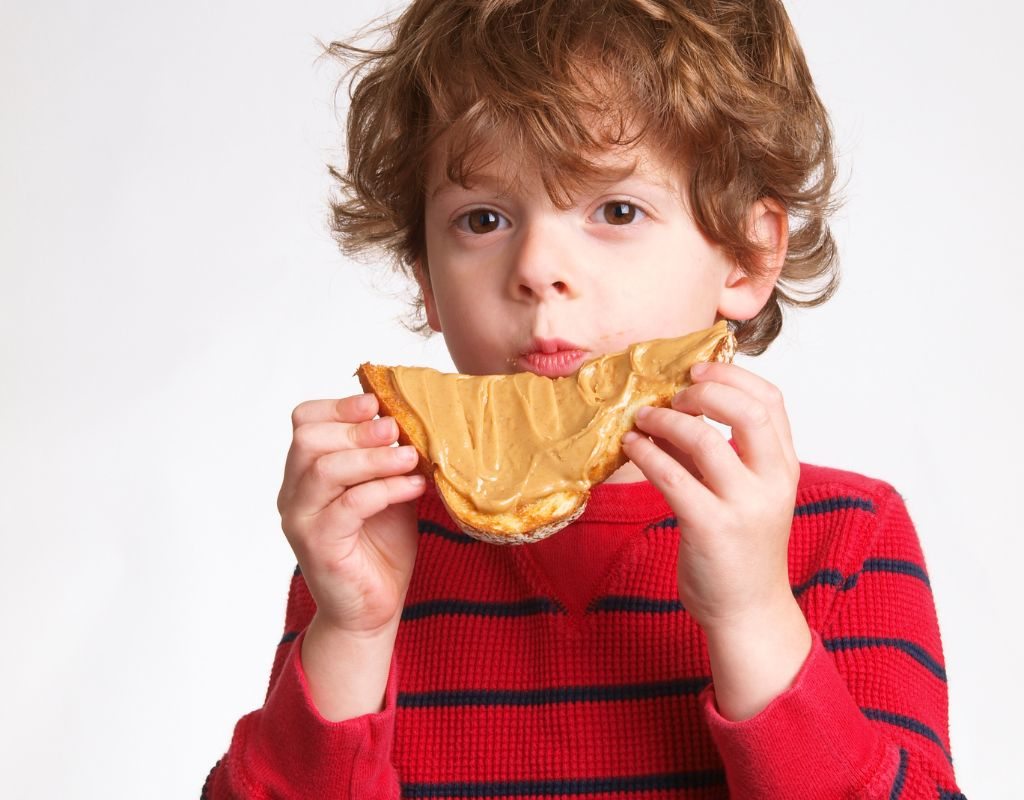 Criança fazendo lanche saudável comendo pão integral com pasta de amendoim