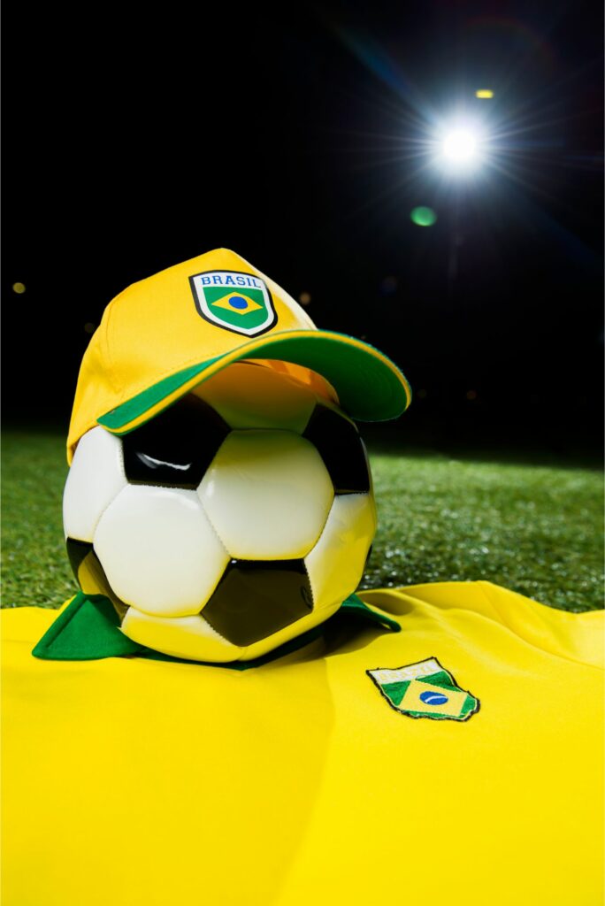 Bola de futebol com boné da seleção brasileira em cima de uma camisa do Brasil.